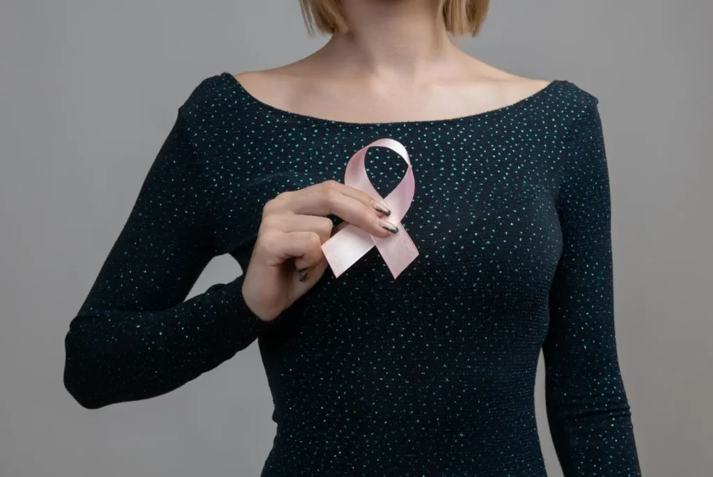 A woman in a black shirt wearing a pink ribbon to symbolize breast cancer awareness