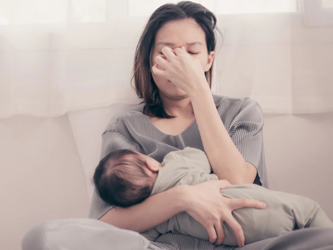 A frustrated mother sitting on her bed breastfeeding her baby
